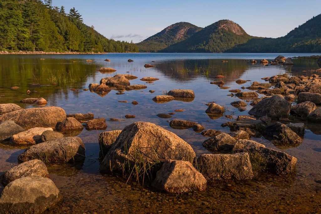 Felsige Flachwasserbereiche des Jordan Pond blicken auf die Zwillingsberge The Bubbles, die sich im ruhigen Wasser des Acadia-Nationalparks spiegeln.